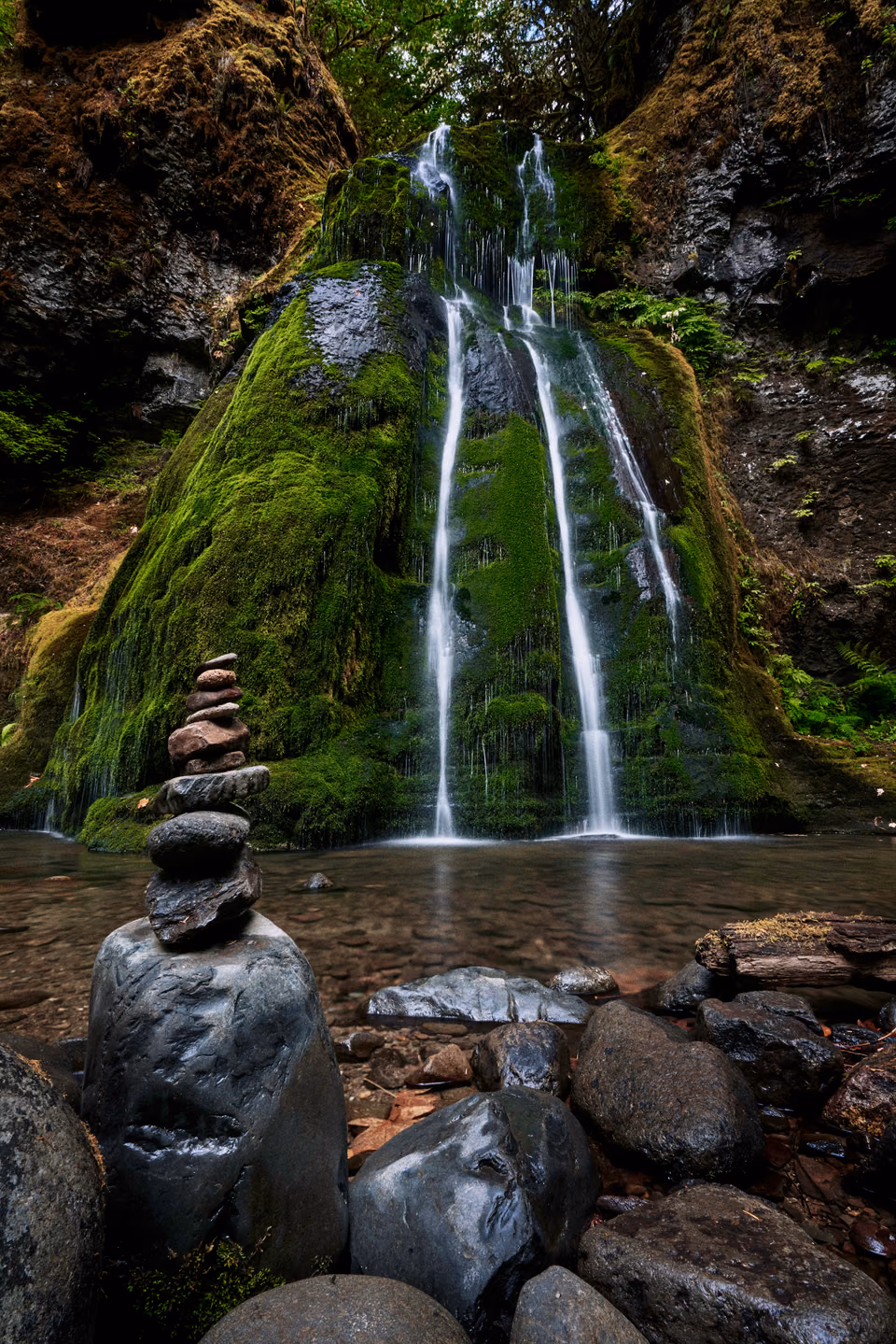 a waterfall cascading over rocks and boulders in a forest
