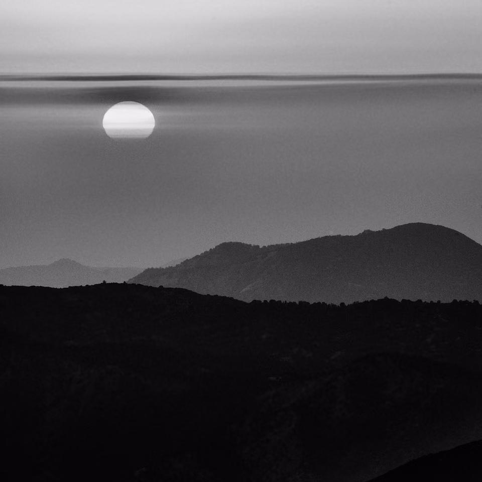 a black and white photo of the sun setting over a mountain
