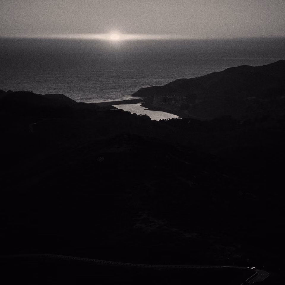 a black and white photo of the sun setting over the ocean

