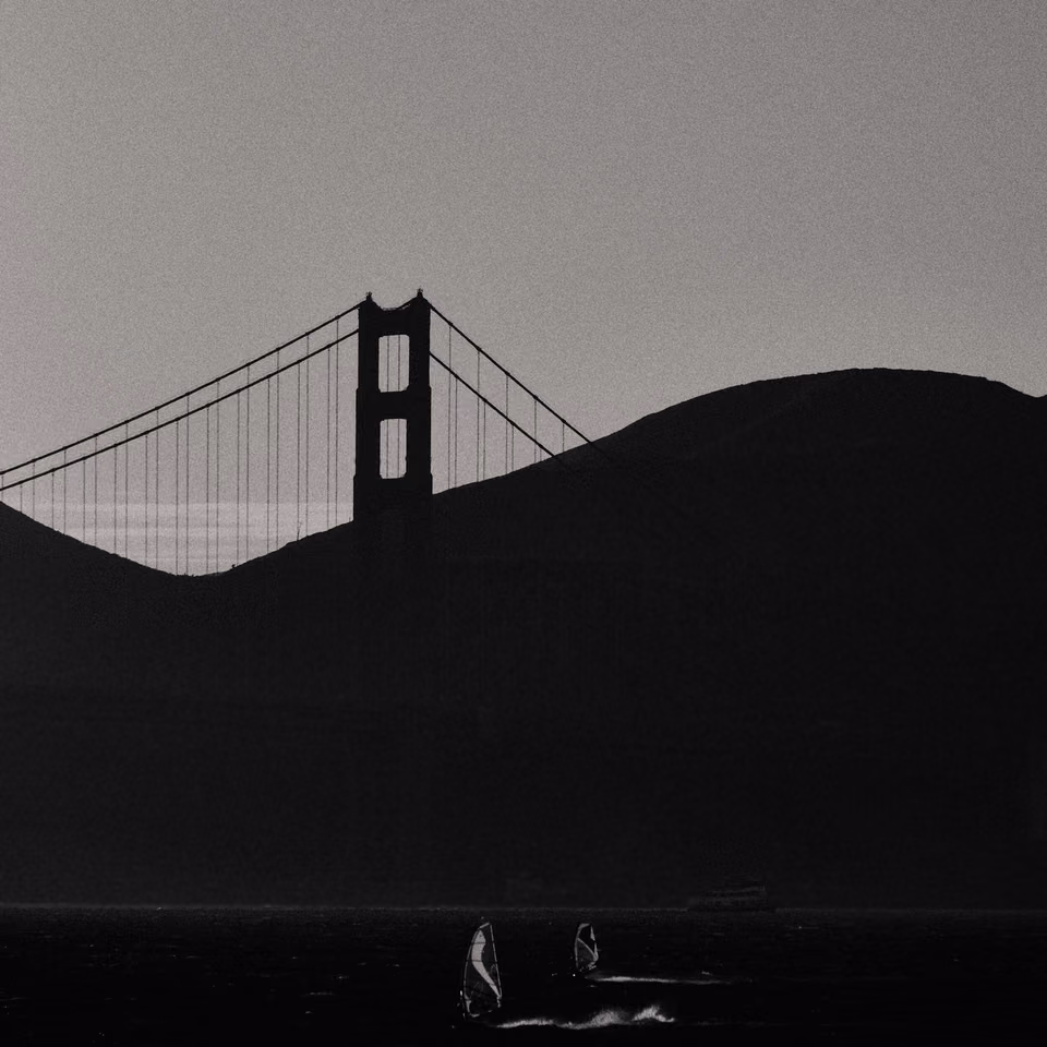 a black and white photo of a sailboat in the water near the golden gate bridge

