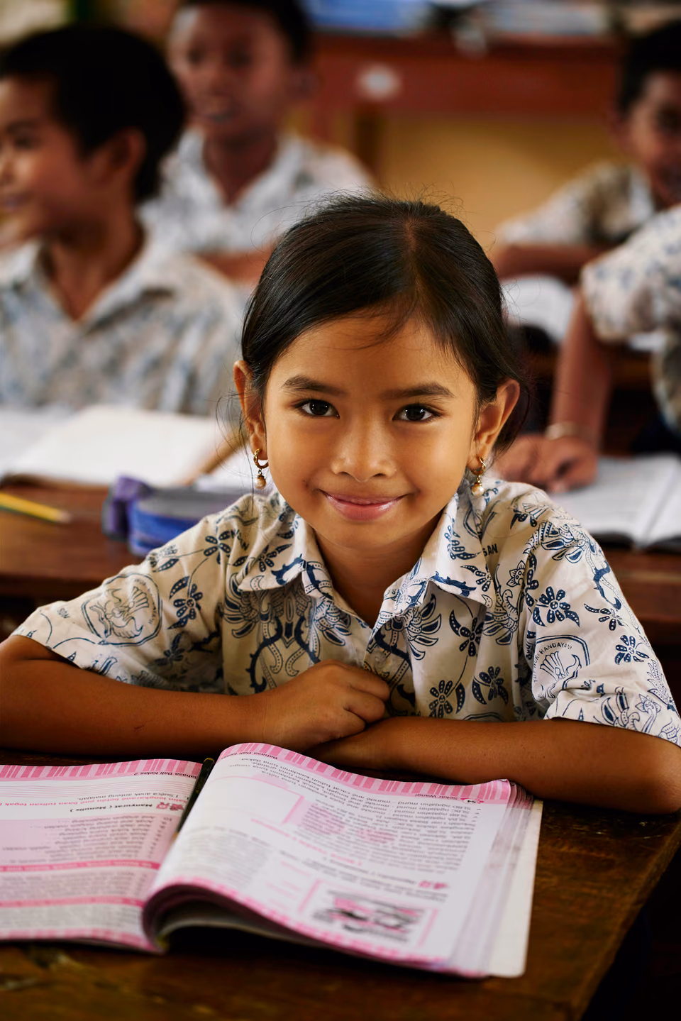 a young girl sitting at a desk with a book

