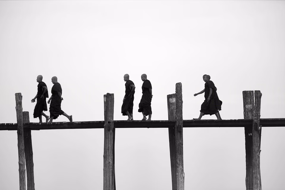 silhouettes of monks walking across a bridge
